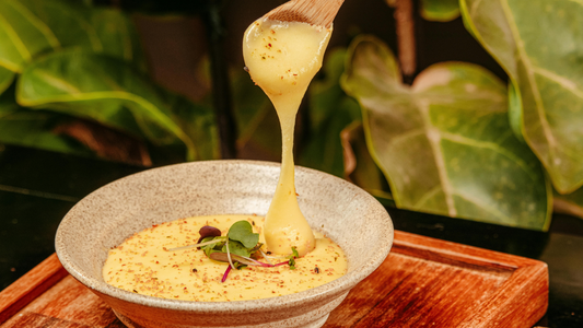 Bowl of creamy honey mustard yogurt dip with herbs and a spoon, surrounded by lemon slices and rustic textures