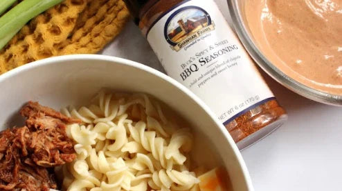 pasta in a bowl with bbq pulled pork, sauce on the side with a bottle of buck's spicy & sweet Seasoning
