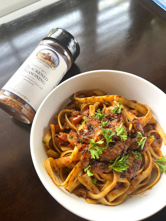 reddish pasta with shrimp and greens in bowl next to a seasoning bottle of blackened seasoning