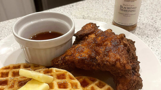 fried chicken on a plate with waffles with pads of butter and a ramekin of maple syrup. 