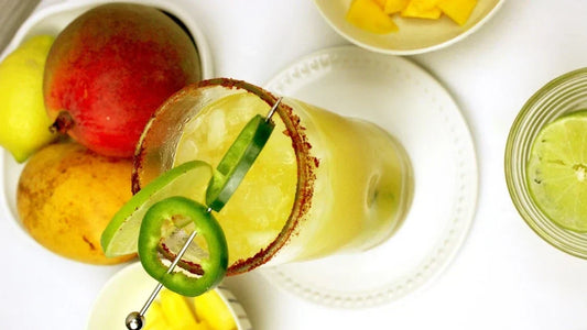 Drink with jalapeno skewer and red seasoned rim on a table. 