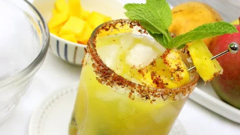 Pineapple drink rimmed with a red seasoning with a pineapple skewer and green garnish