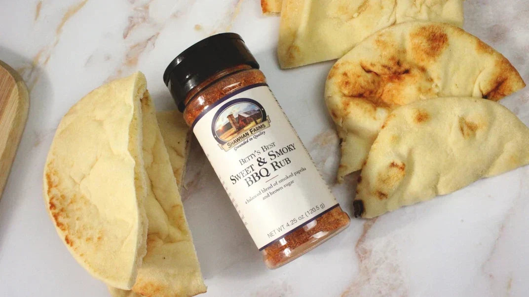 A bottle of Betty's Best BBQ seasoning next to pita bread / chips on the counter. 