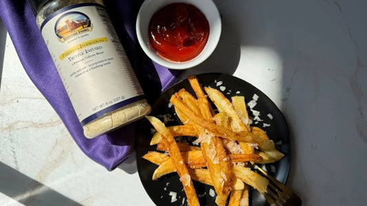 Fries on a black plate with parmesan sprinkled over, ketchup in a small ramekin as well as Truffle Parm seasoning blend. 