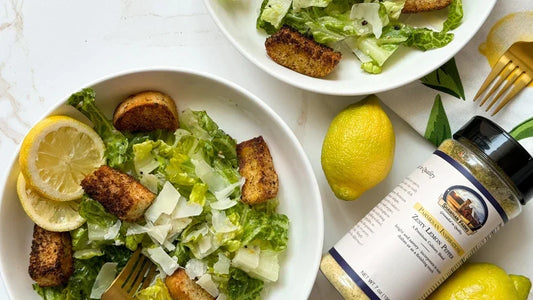 Lettuce in a bowl with lemon slices, croutons and a bottle of lemon pepper parmesan off to the side. 