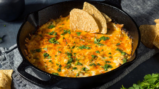 A cast iron skillet with melted cheese, tortilla chips and cilantro as a garnish