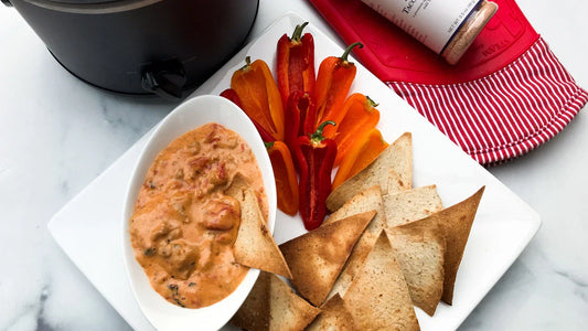 Sliced Bell peppers next to pita chips on a plate with a bowl of taco dip