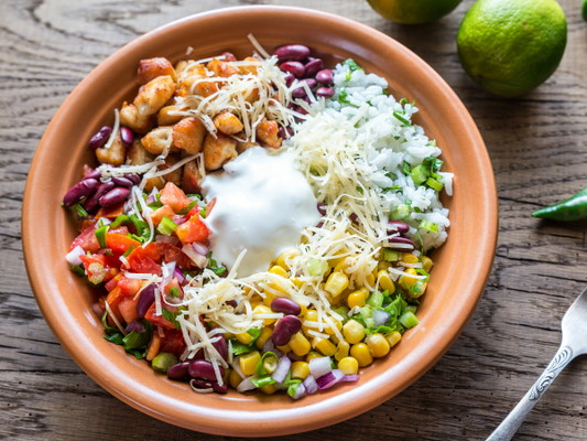 Corn, onion, chicken, tomato, beans, and herbs with cheese and sour cream in a bowl