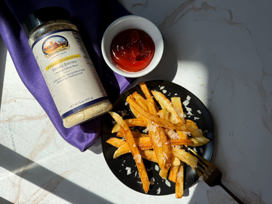 Golden crispy Parmesan truffle fries topped with shredded Parmesan, served as a gourmet side dish or snack. A bottle of Shawhan Farms Truffle Parmesan is next to the plate. Image courtesy of My Curated Tastes.