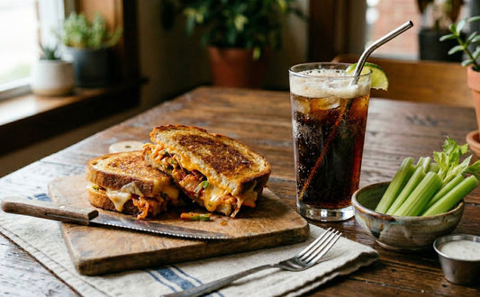 red and cheesy grilled cheese on a cutting board with a glass of soda and celery sticks on the side. 