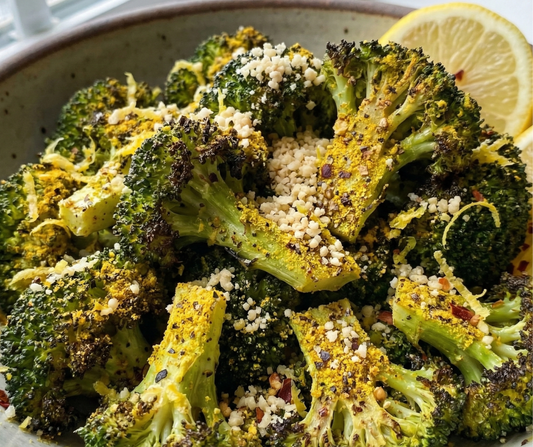 Broccoli in a bowl with lemon pepper parm seasoning on it and lemon slices.