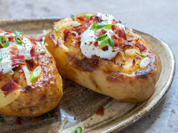 Baked potato on a plate with sour cream, green onion, bacon, and cheese