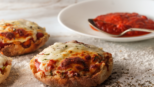 Muffins with melted cheese and tomato sauce with a plate of tomato sauce and a spoon behind it. 