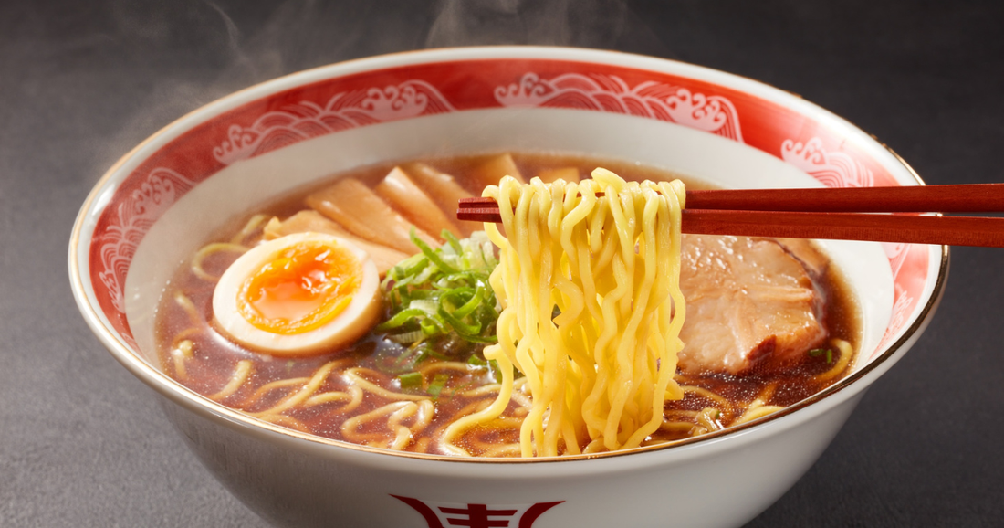Holding ramen noodles with chopsticks with a jammy egg and pork slices in the ramen bowl