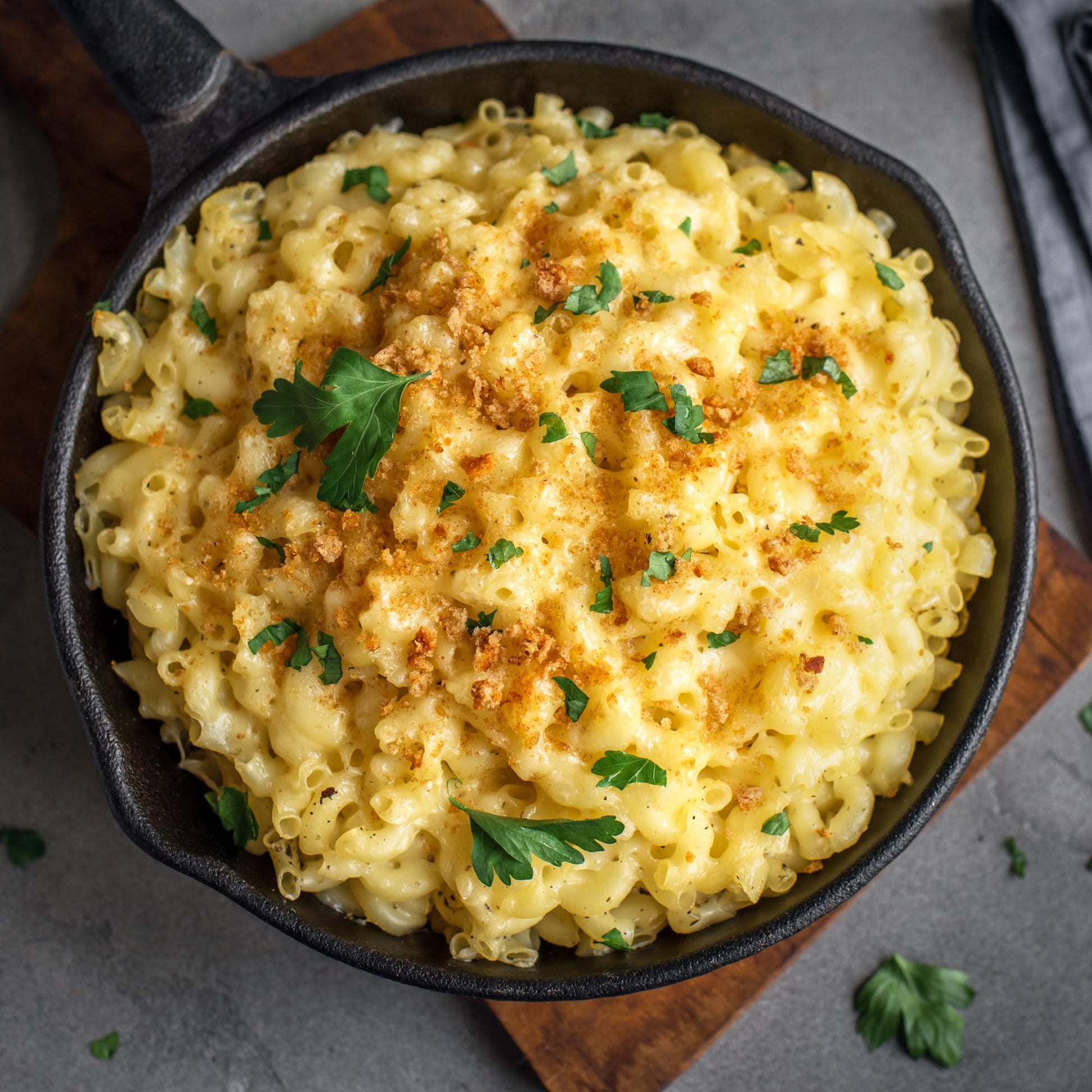 Cast Iron Skillet with Mac N Cheese, crumbs, parsley on a cutting board. 